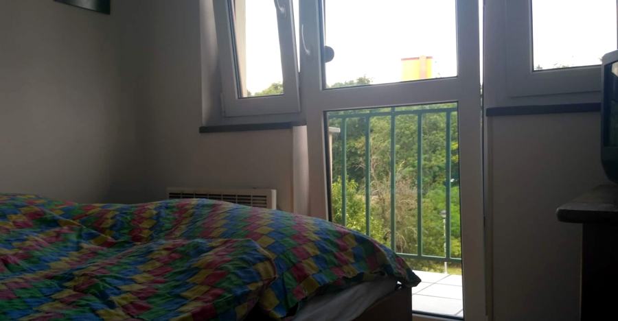 Postel u okna, venku zábradlí balkonu a zeleň