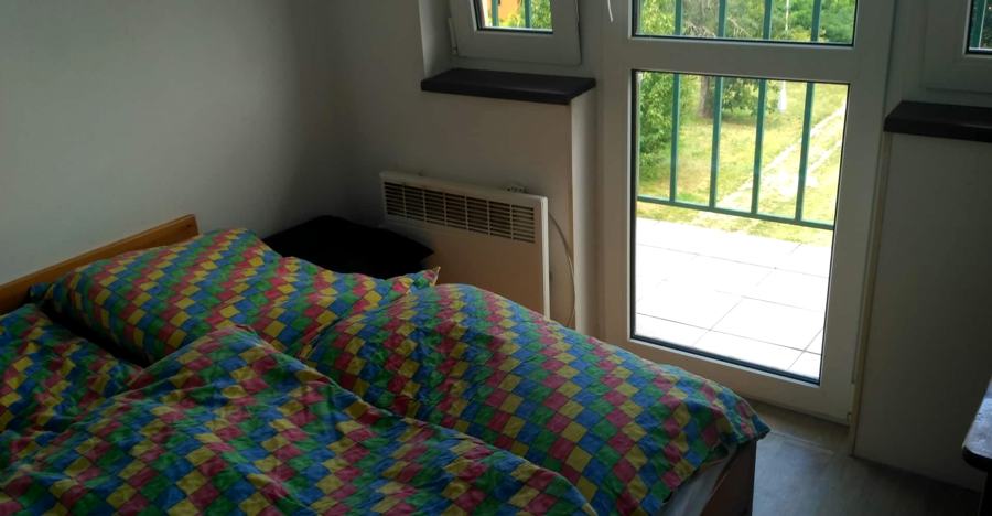 Ložnice s manželskou postelí a barevným přehozem, prosklené dveře na balkon